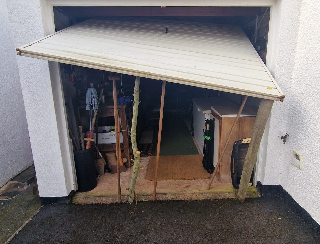 A garage door propped open with broom sticks and branches until the cables can be replaced.